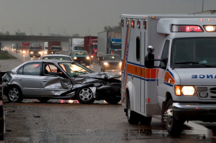 Crashed silver car on highway with ambulance next to it